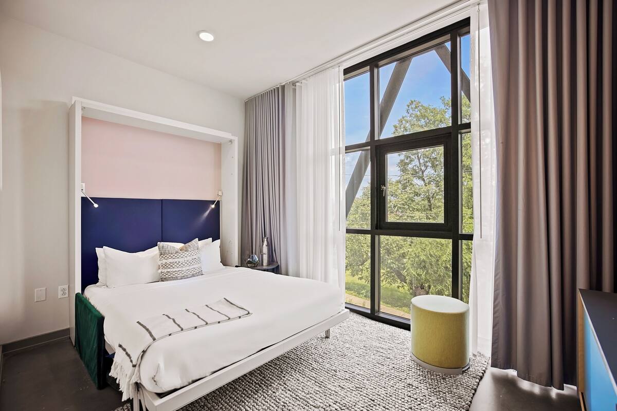 Une chambre d’hôtel moderne avec un grand lit, une vue sur la verdure et une fenêtre avec des rideaux.