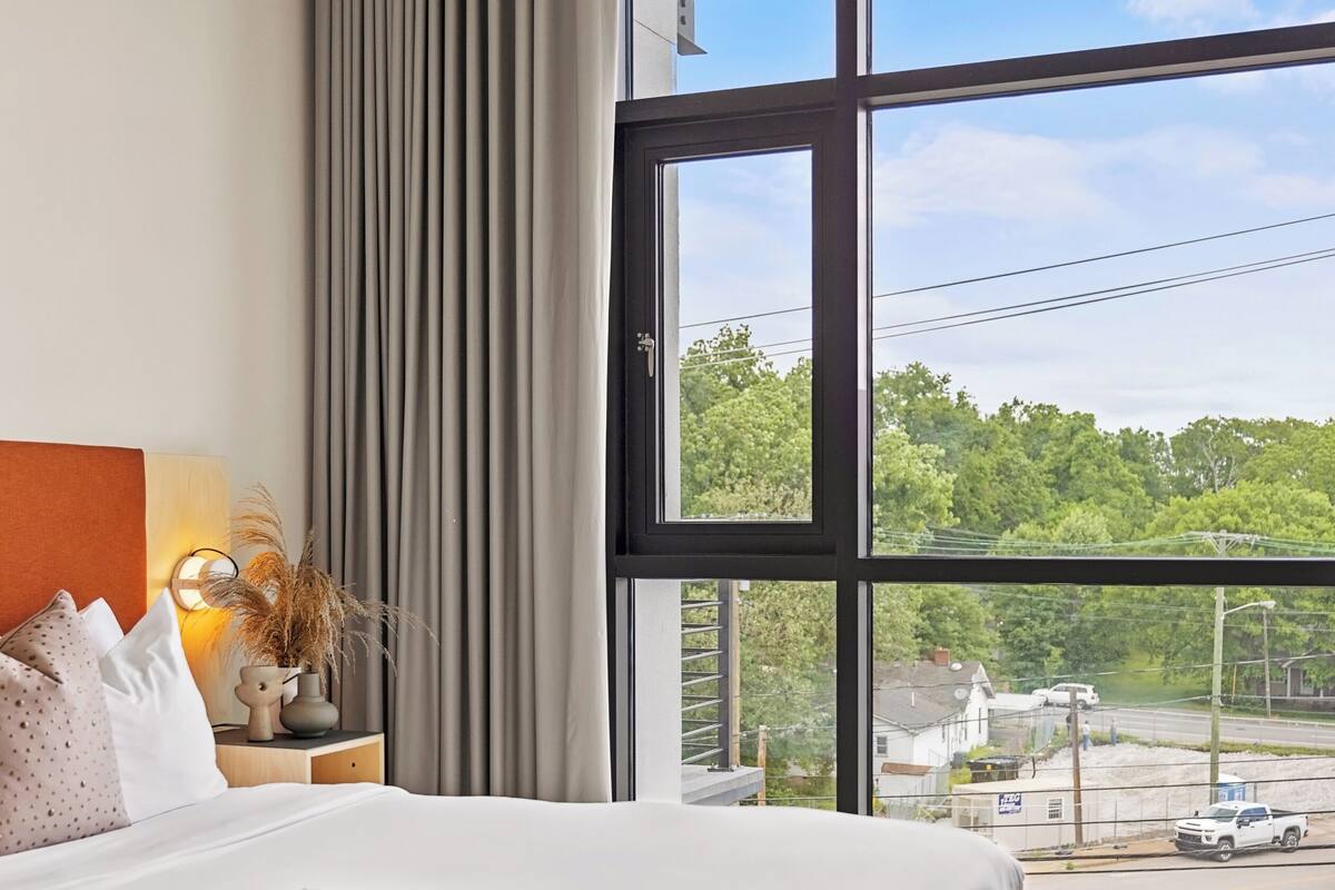 Une chambre avec une grande fenêtre, un lit, une table de chevet et une vue sur la rue.