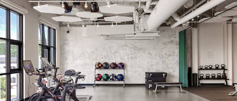 Une salle de sport équipée de vélos d’exercice, d’un support mural où sont rangées des balles d’exercice de différentes couleurs, et de kettlebells.