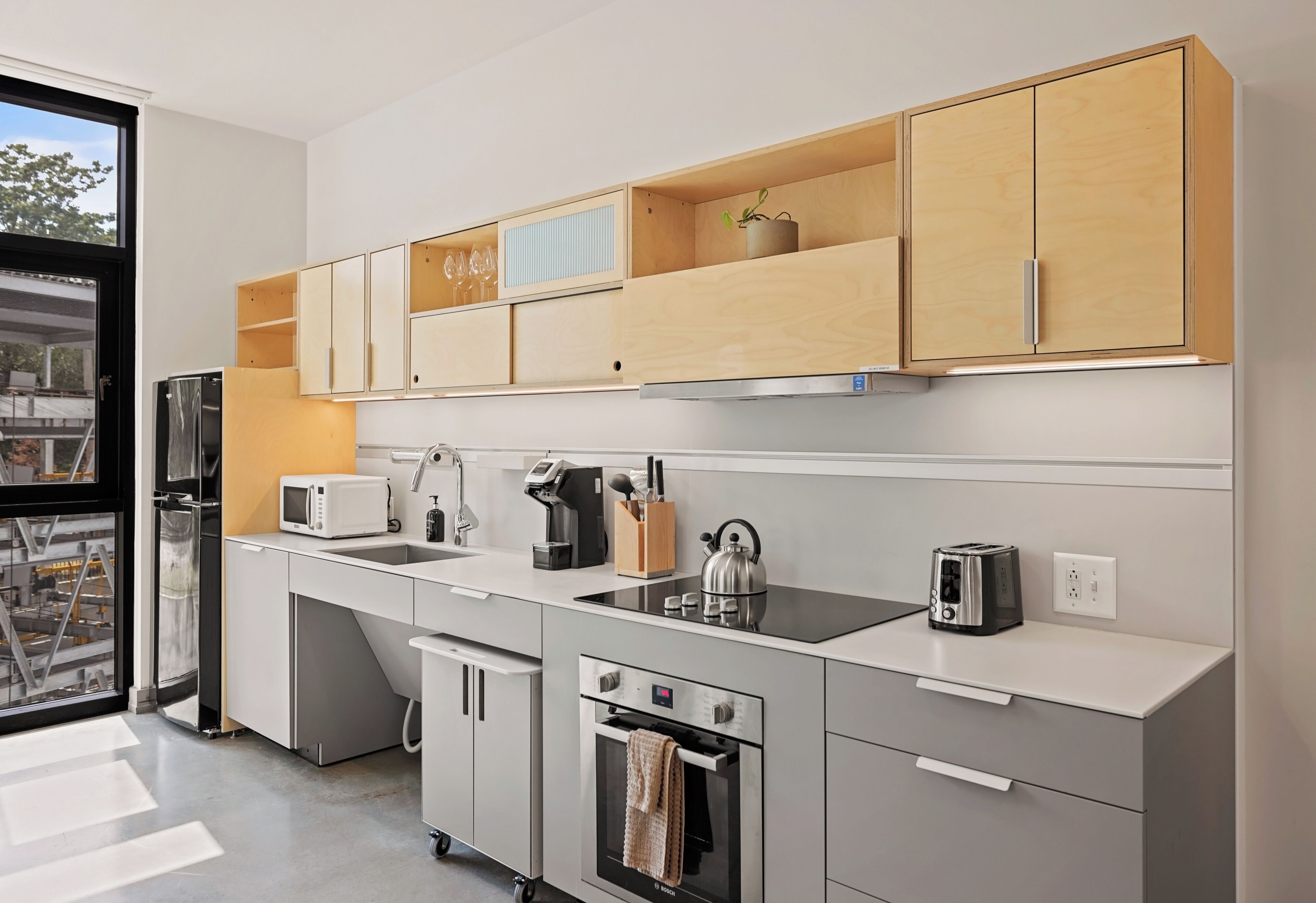 A modern kitchen with a built-in oven, microwave, and toaster, wooden cabinets, and a window with a view of the outside.