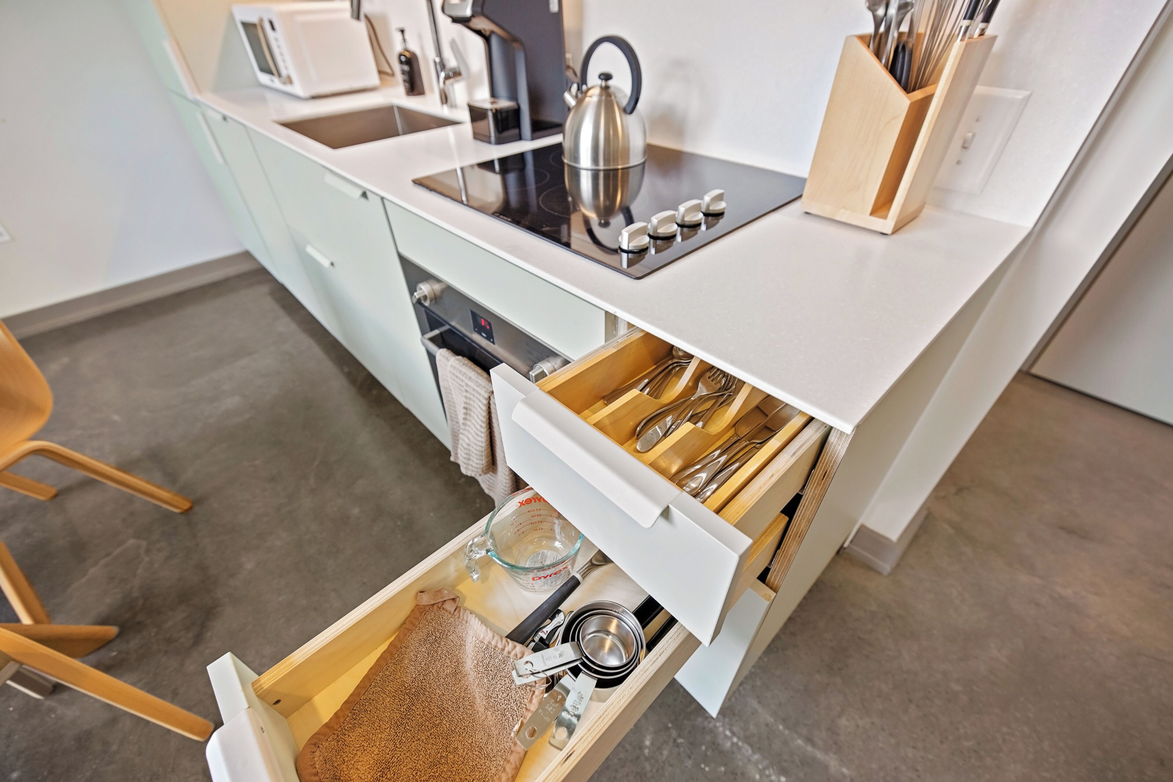 A kitchen with a built-in microwave, kettle, and a drawer with utensils and measuring cups.