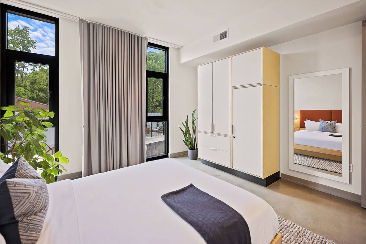 Une chambre d’hôtel moderne avec un grand lit, une armoire, une plante en pot et une vue sur l’extérieur.