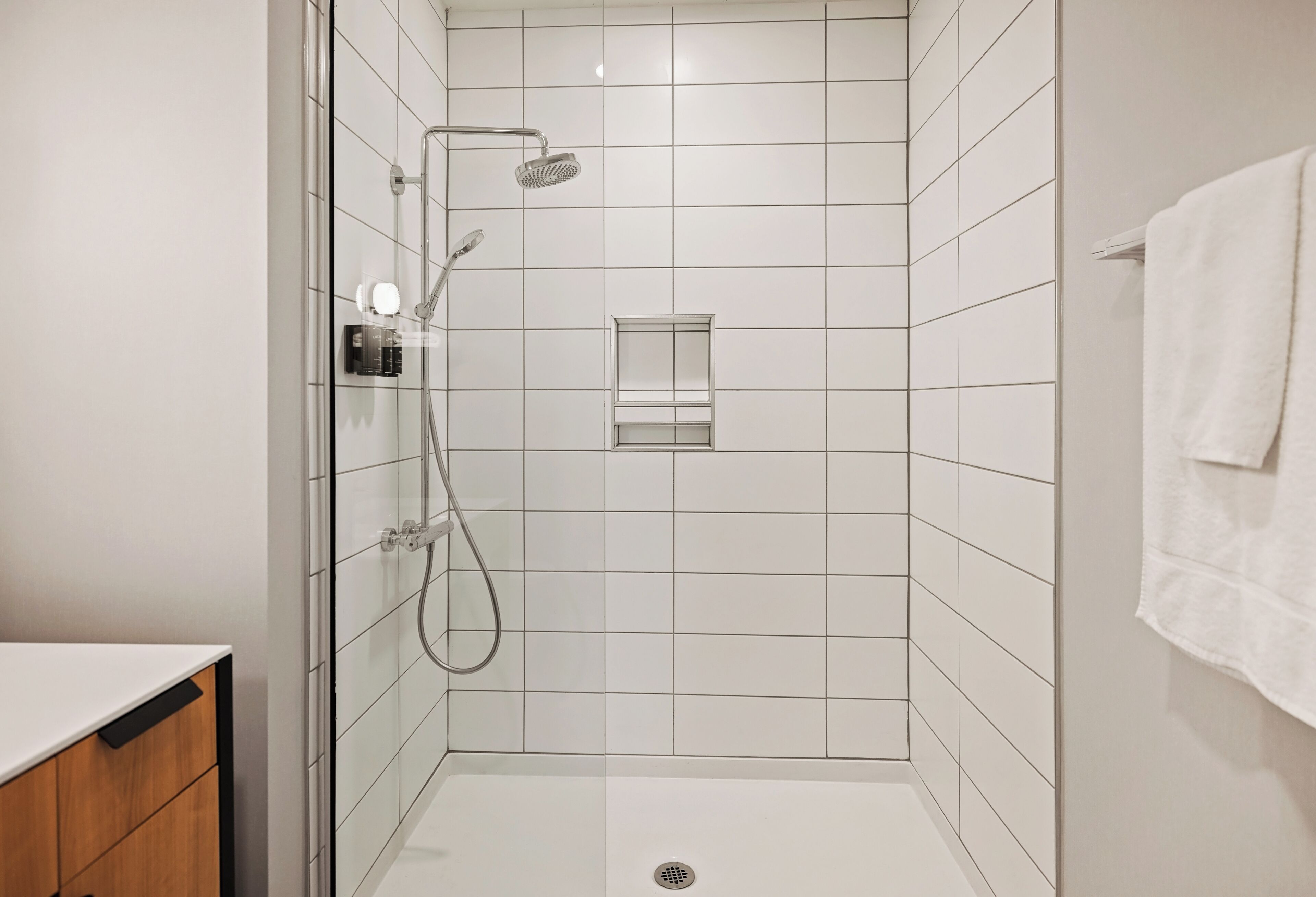 Un baño moderno con cabina de ducha de vidrio, paredes de azulejos blancos y una toalla blanca colgada en la pared.