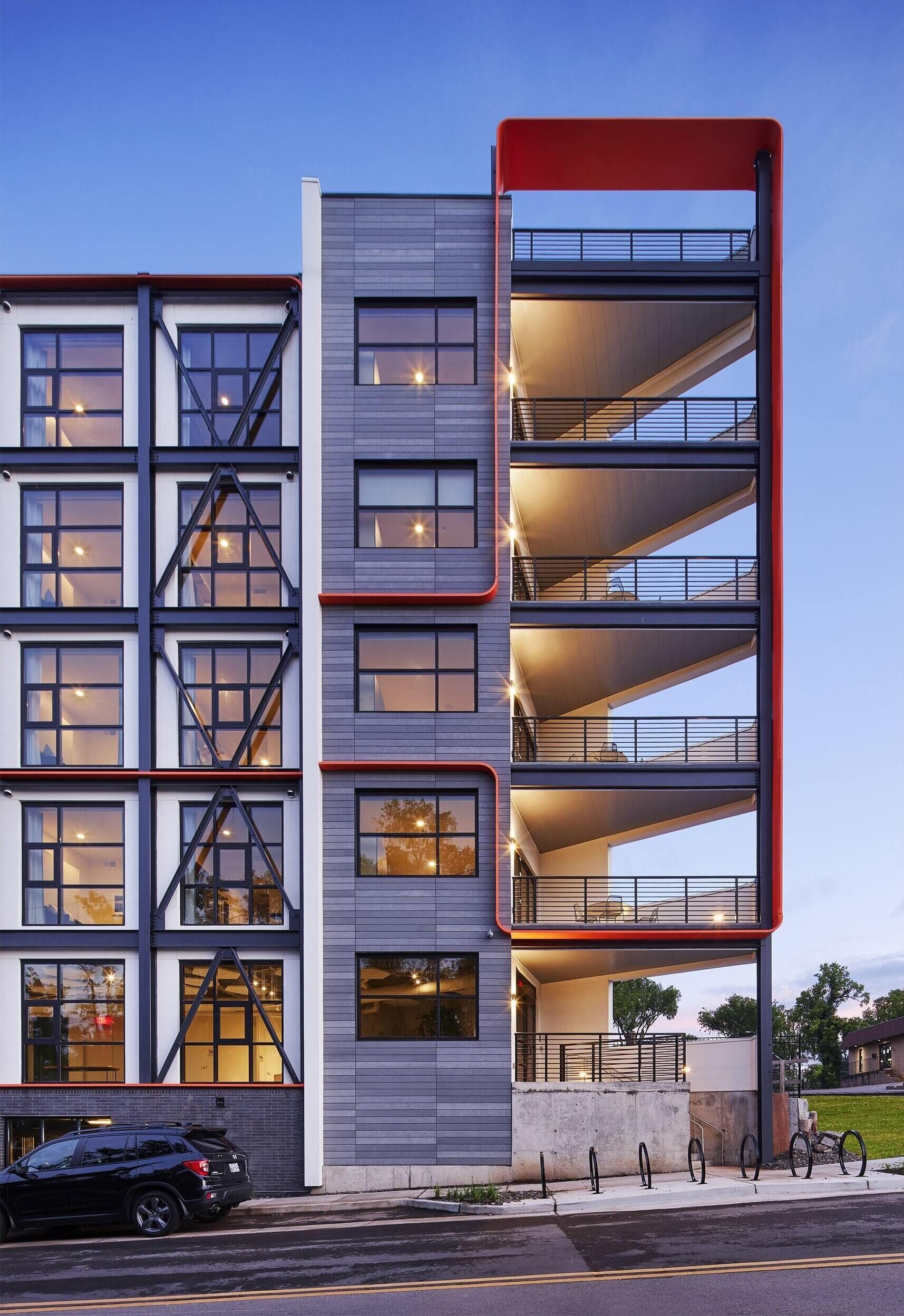 En byggnad med flera våningar och en modern arkitektonisk design, med balkonger och en parkeringsplats.