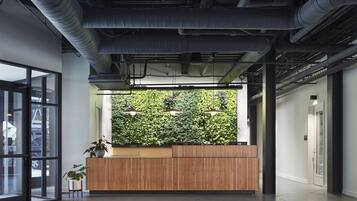 An indoor reception area with a wooden reception desk, a green wall with plants, and a glass door leading outside.