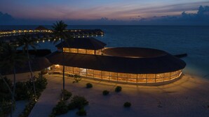 Un complexe hôtelier doté de bungalows sur pilotis, d’un bâtiment circulaire et d’une plage.