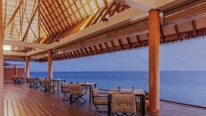 Une terrasse en bois, avec des tables et des chaises, donnant sur la mer.