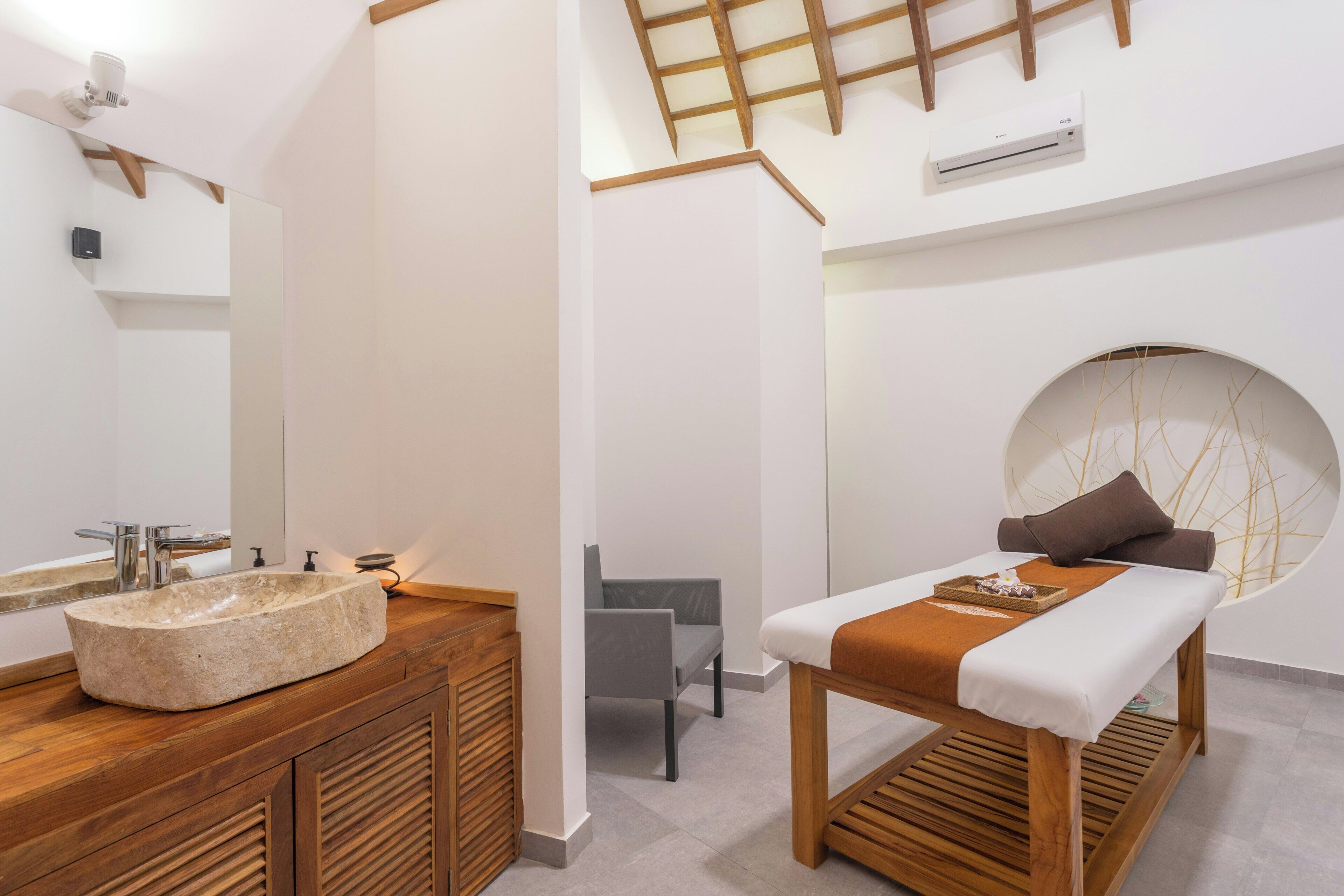 A modern bathroom with a stone sink, wooden vanity, a massage table, and a round bathtub.