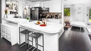 A modern kitchen with a central island, stainless steel appliances, and a dining area with a sofa and table. - 5 room TampaGolfVillas by AmericanVacationLiving (Wesley Chapel)