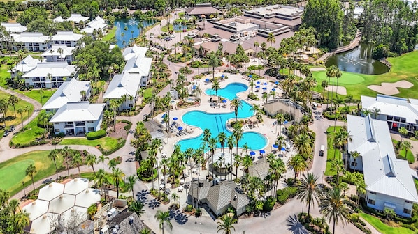 An aerial view of a resort with multiple swimming pools, palm trees, and resort buildings.