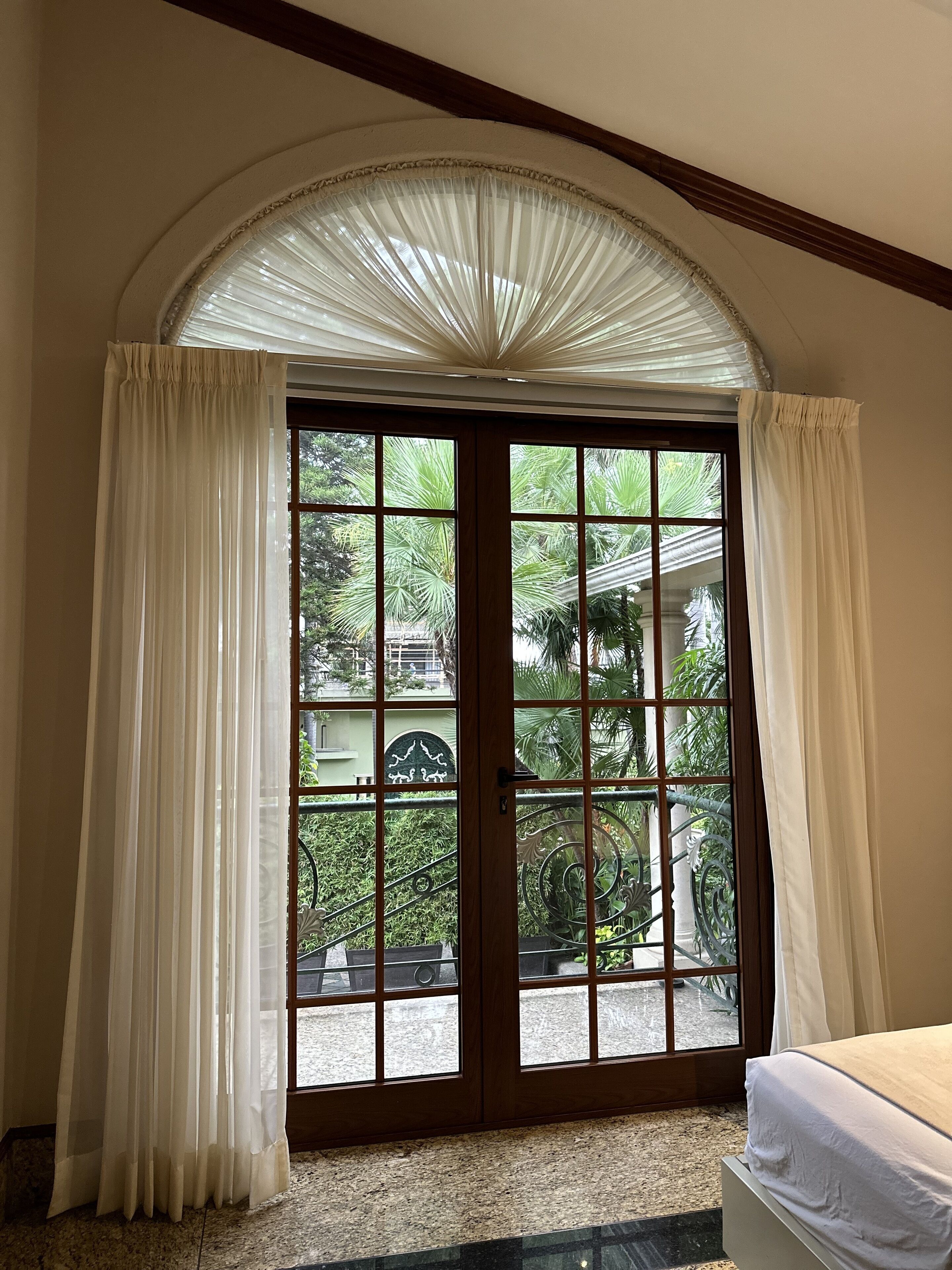 A room with a large sliding glass door leading to a balcony, a bed with a white bedspread, and a carpeted floor.