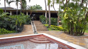 A pool area with tiled flooring, palm trees, and a staircase leading to a building.