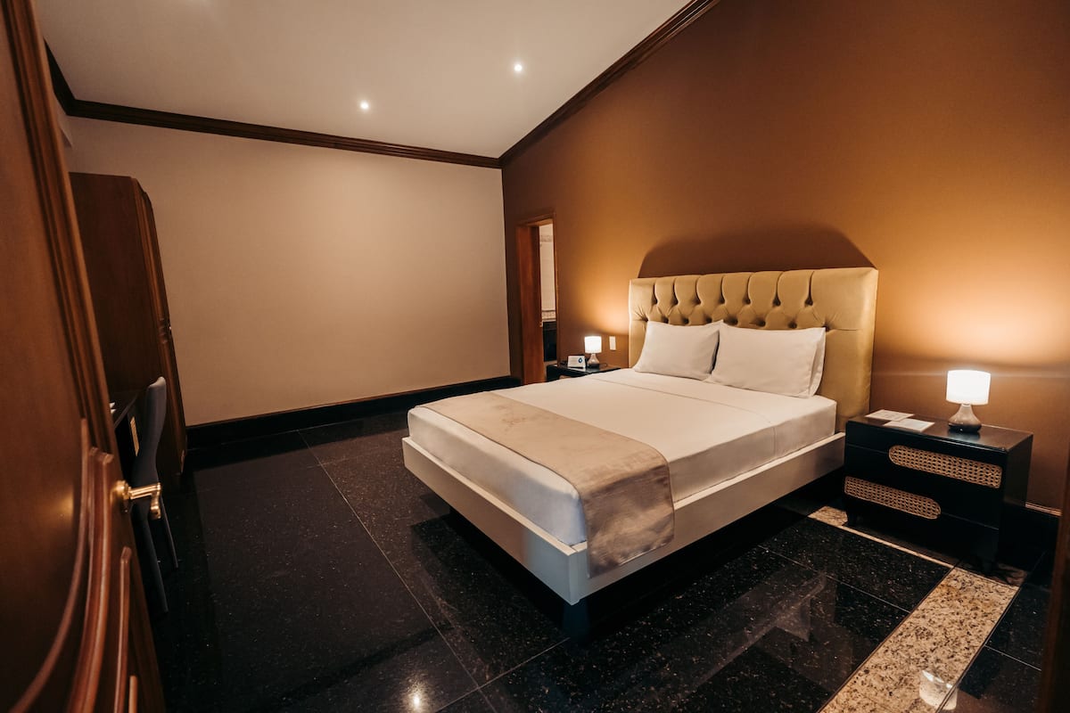 Ein Hotelzimmer mit einem großen Bett, einem Nachttisch mit Lampe und einer Holztür.