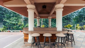 An outdoor bar area with a wooden ceiling, white columns, and a stone counter.