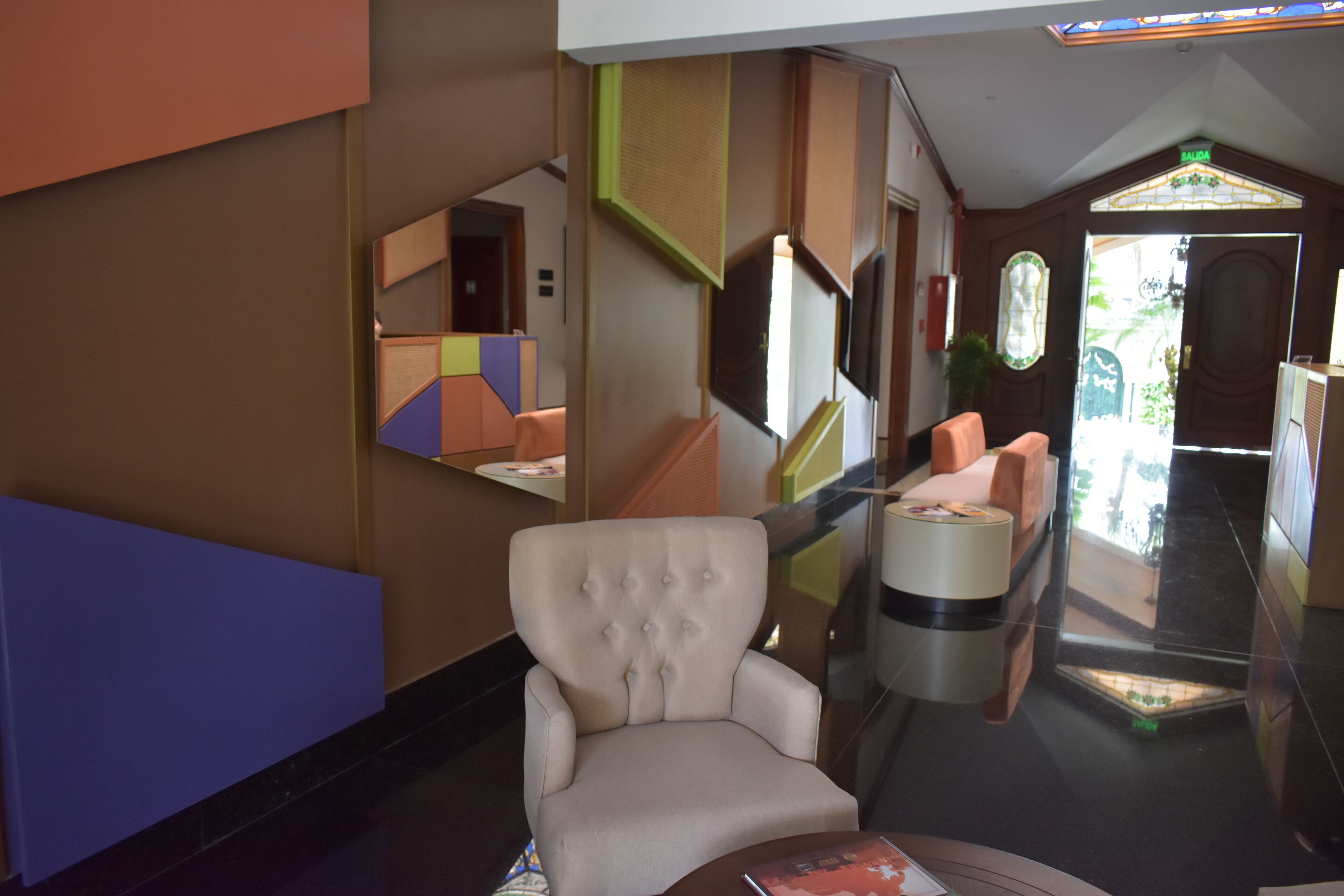 A lobby with a plush armchair, a round table, and a mirror reflecting the room.
