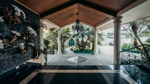 A covered outdoor area with a wooden ceiling, columns, and a decorative wall with white flowers.