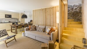 En moderne stue med sofa, sofabord og spiseområde. En trappe med træbeklædning fører til en etage ovenover.