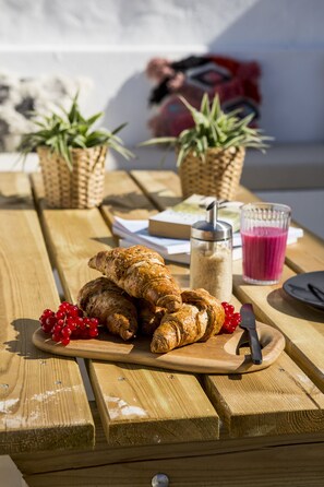 Una mesa de picnic de madera con cruasanes, grosellas rojas, un vaso de jugo y una botella de leche.