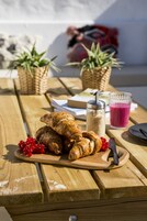 Uma mesa de piquenique de madeira com croissants, groselhas vermelhas, um copo de suco e uma garrafa de leite.