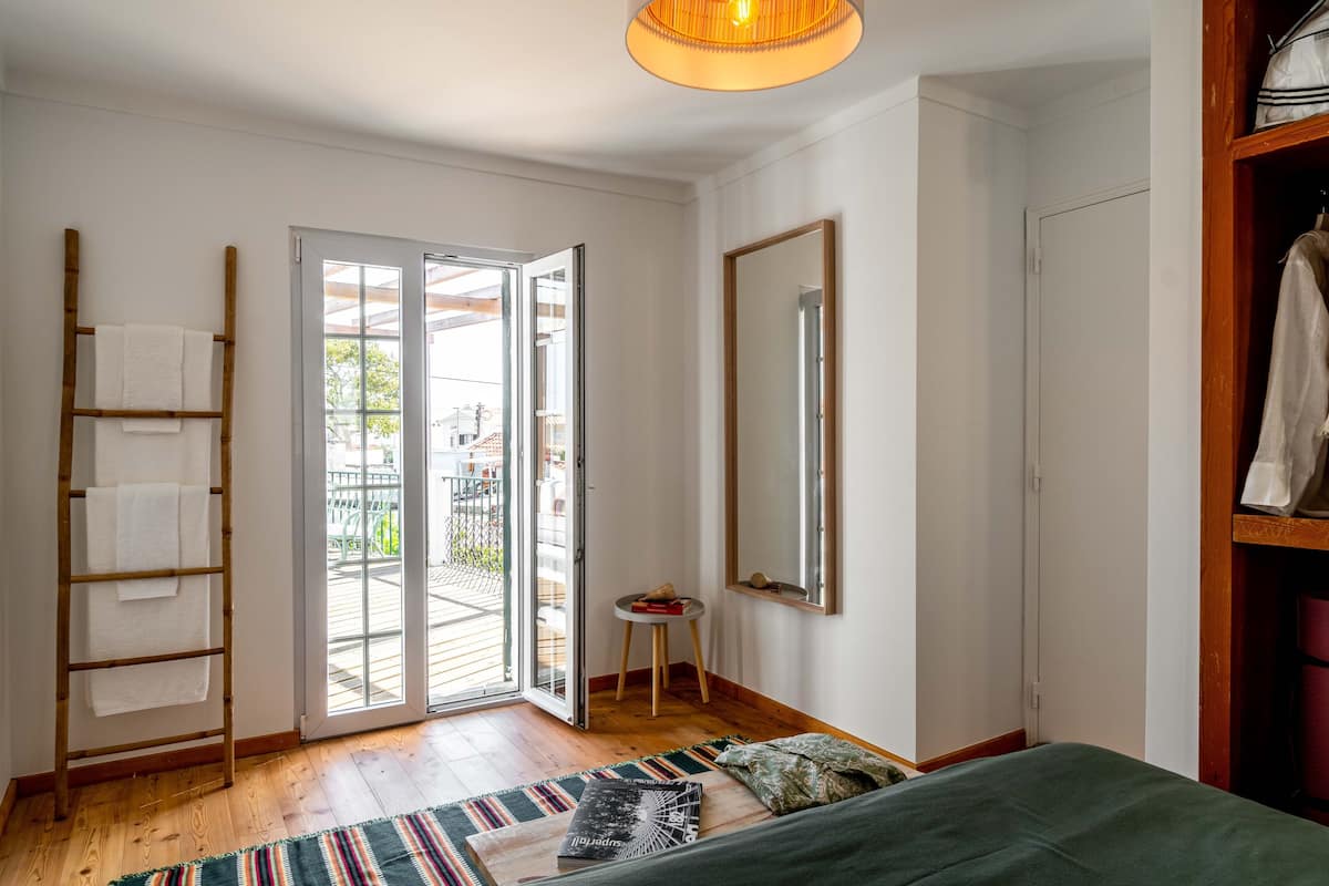 Ein Schlafzimmer mit einem Bett, einer Holzleiter mit Handtüchern, einem kleinen Hocker, einem Spiegel und einem Kleiderschrank.