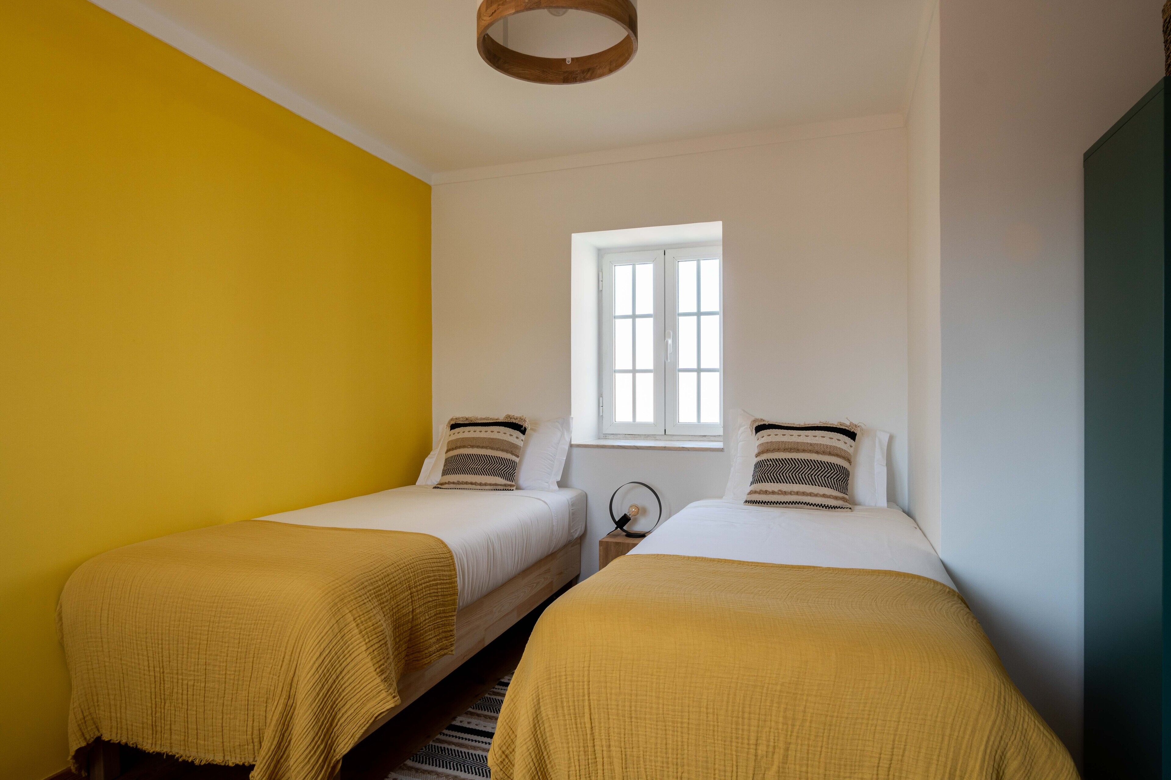Quarto com duas camas, uma janela e um lustre de madeira.