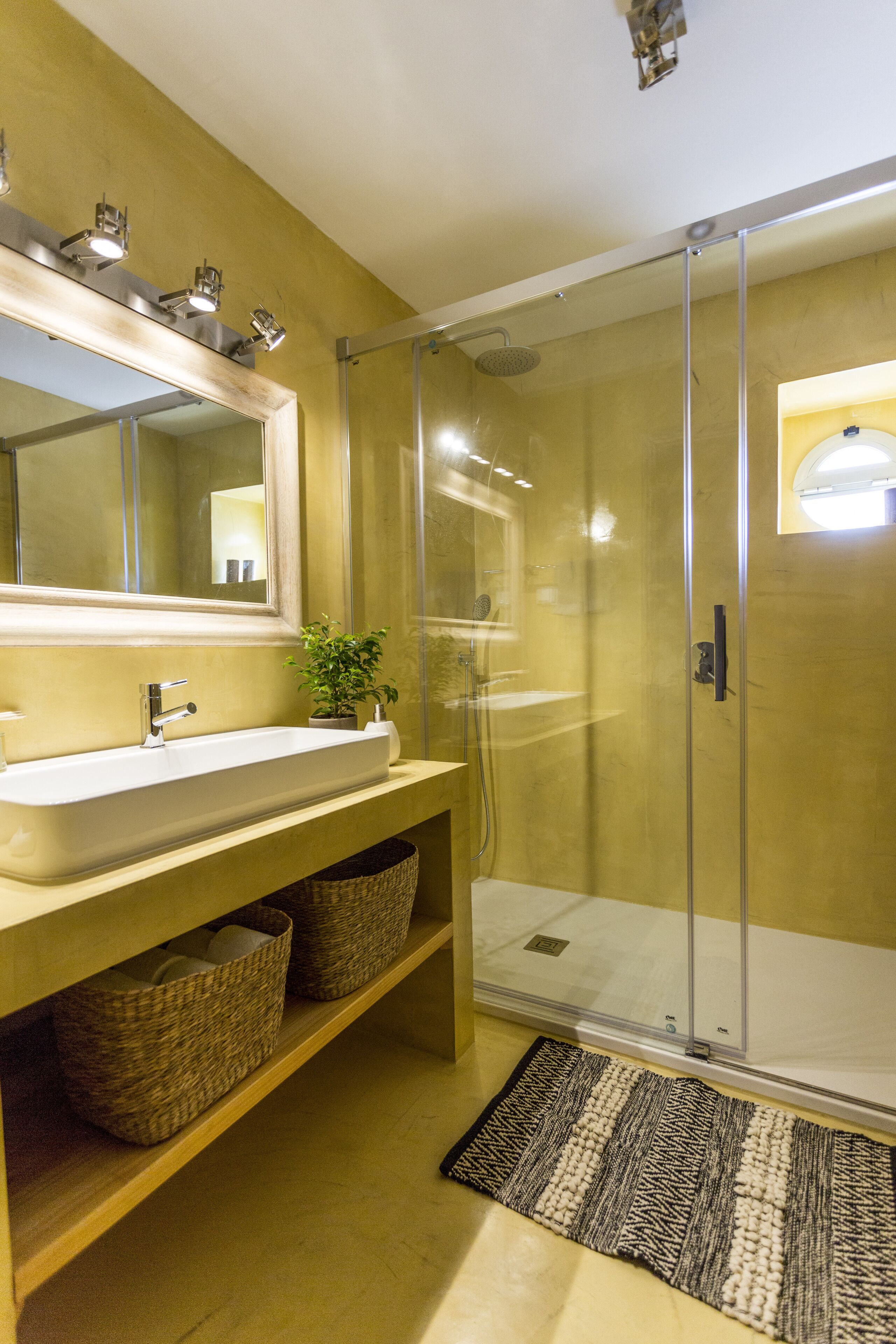 Ein Badezimmer mit einem großen Spiegel, einem Waschbecken, einer Dusche und Körben aus Weidengeflecht auf der Ablagefläche.