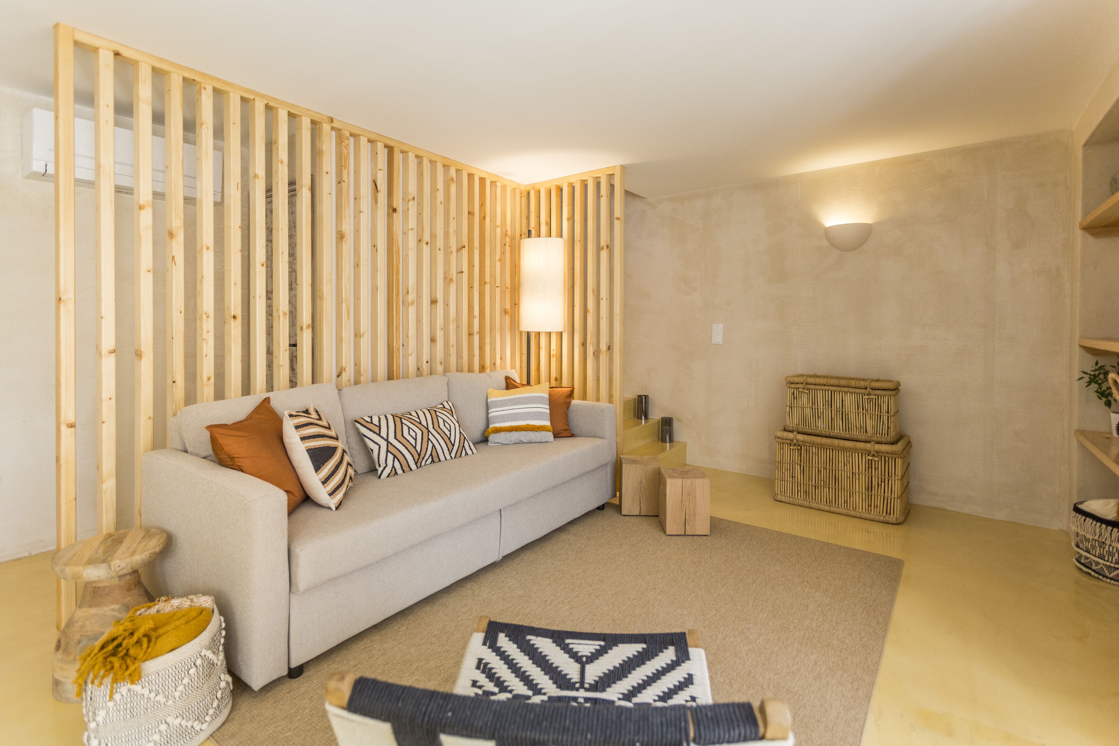 A living room with a sofa, cushions, a lamp, a small table, and a basket.
