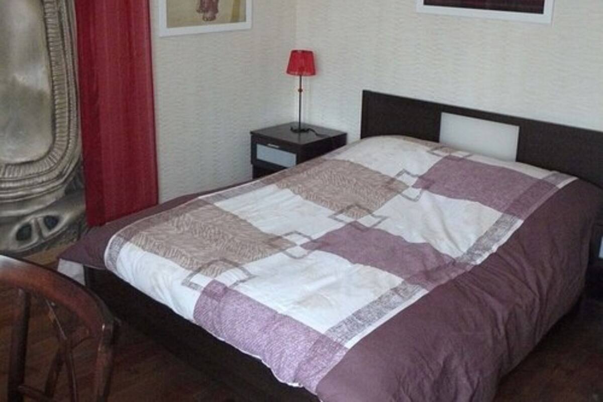 A bedroom with a bed, a nightstand, a lamp, and a chair.