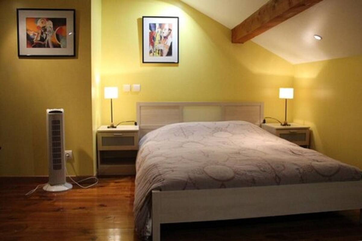 A bedroom with a bed, two bedside tables, two wall-mounted lamps, a standing heater, and two framed pictures on the wall.