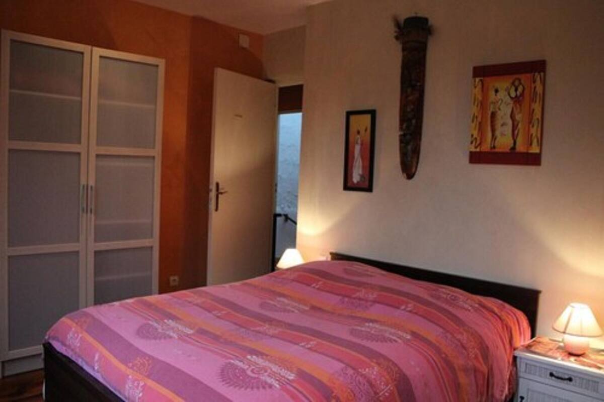 A bedroom with a bed, a nightstand, a lamp, a wardrobe, and two framed pictures on the wall.