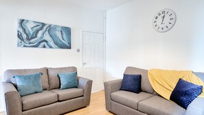 Two grey sofas with blue and yellow cushions, a marble artwork, and a wall clock. - Great Space in Morriston (Swansea)