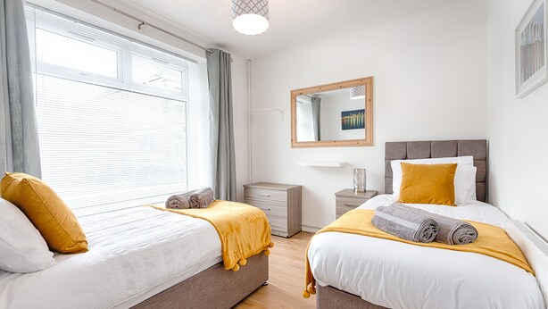 A hotel room with two beds, a bedside table, a nightstand, a mirror, and a window with curtains. - Great Space in Morriston (Swansea)