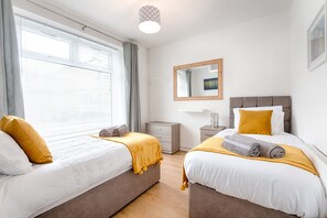Une chambre d’hôtel avec deux lits, une table de chevet, une commode, un miroir et une fenêtre avec des rideaux.