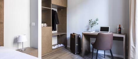 Habitación de hotel con cama, escritorio con una computadora portátil, maleta, silla, lámpara y armario.