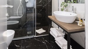 Un baño moderno con ducha de vidrio, lavamanos blanco y suelo de mármol.