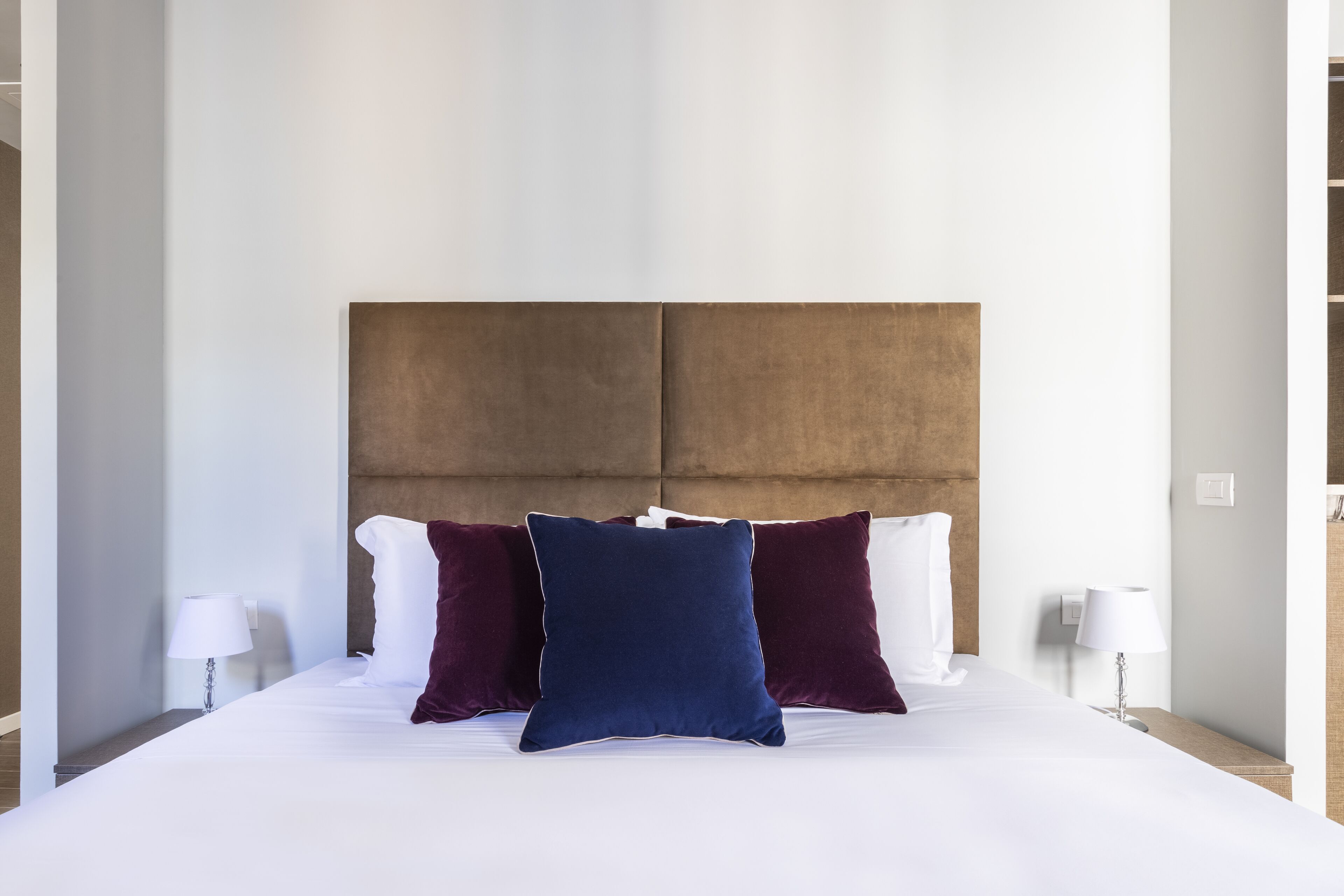 Hotellihuone, jossa on suuri sänky, pääty, kaksi yöpöytävalaisinta ja yöpöytä.