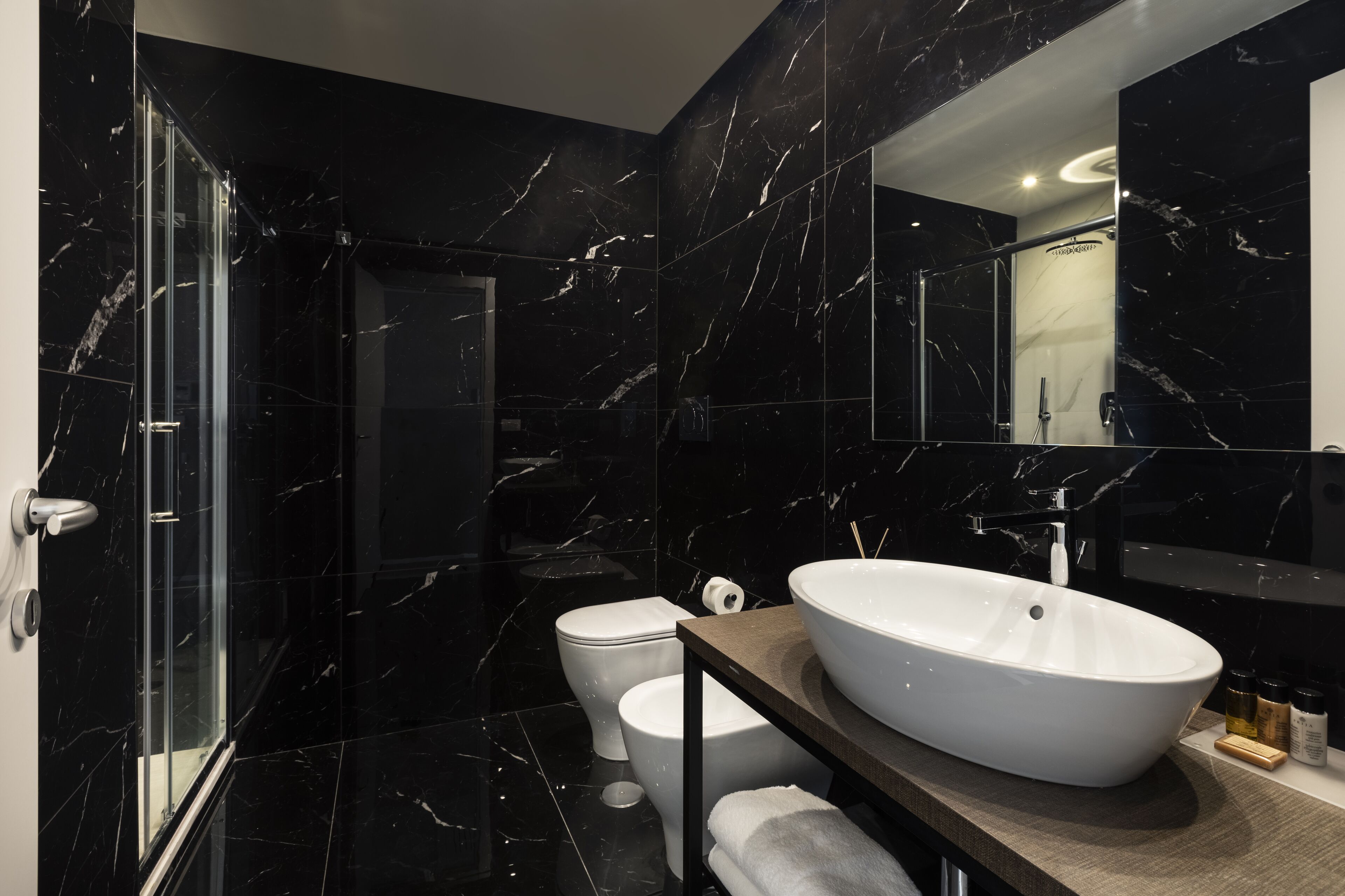 Un bagno moderno con un ampio lavabo bianco, una cabina doccia in vetro e un pavimento in marmo.