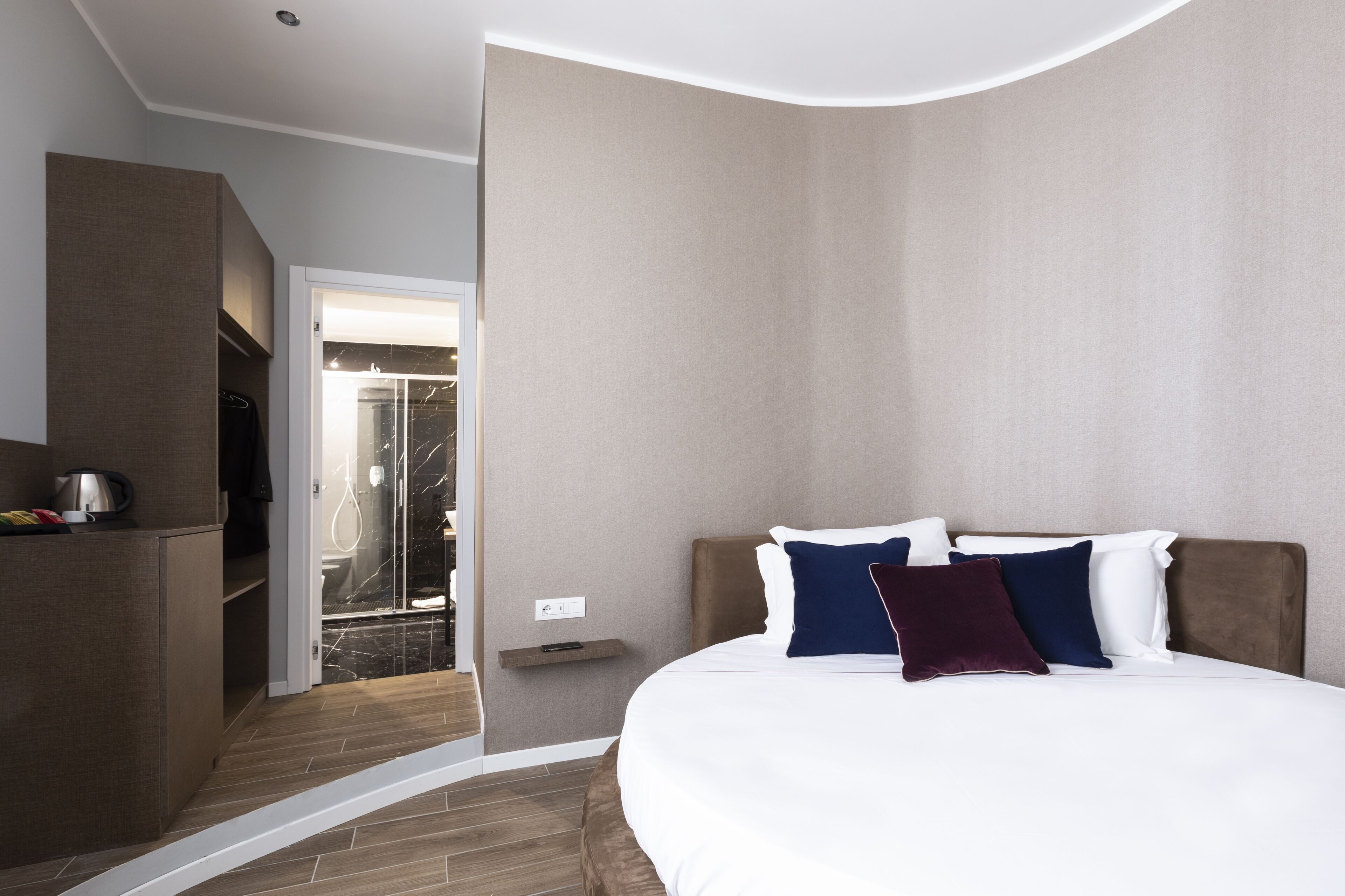 Ein modernes Hotelzimmer mit einem großen Bett, einer eingebauten Garderobe und einer Duschkabine.