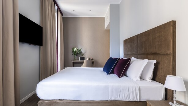 Una habitación de hotel moderna con una cama grande, un televisor de pantalla plana en la pared y una mesita de noche con lámpara.