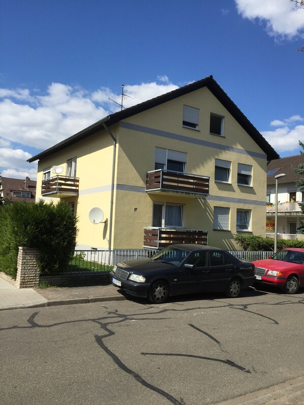 A multi-story building with balconies, a parking area, and a red car parked nearby. - Pension Knielingen Karlsruhe (Karlsruhe)