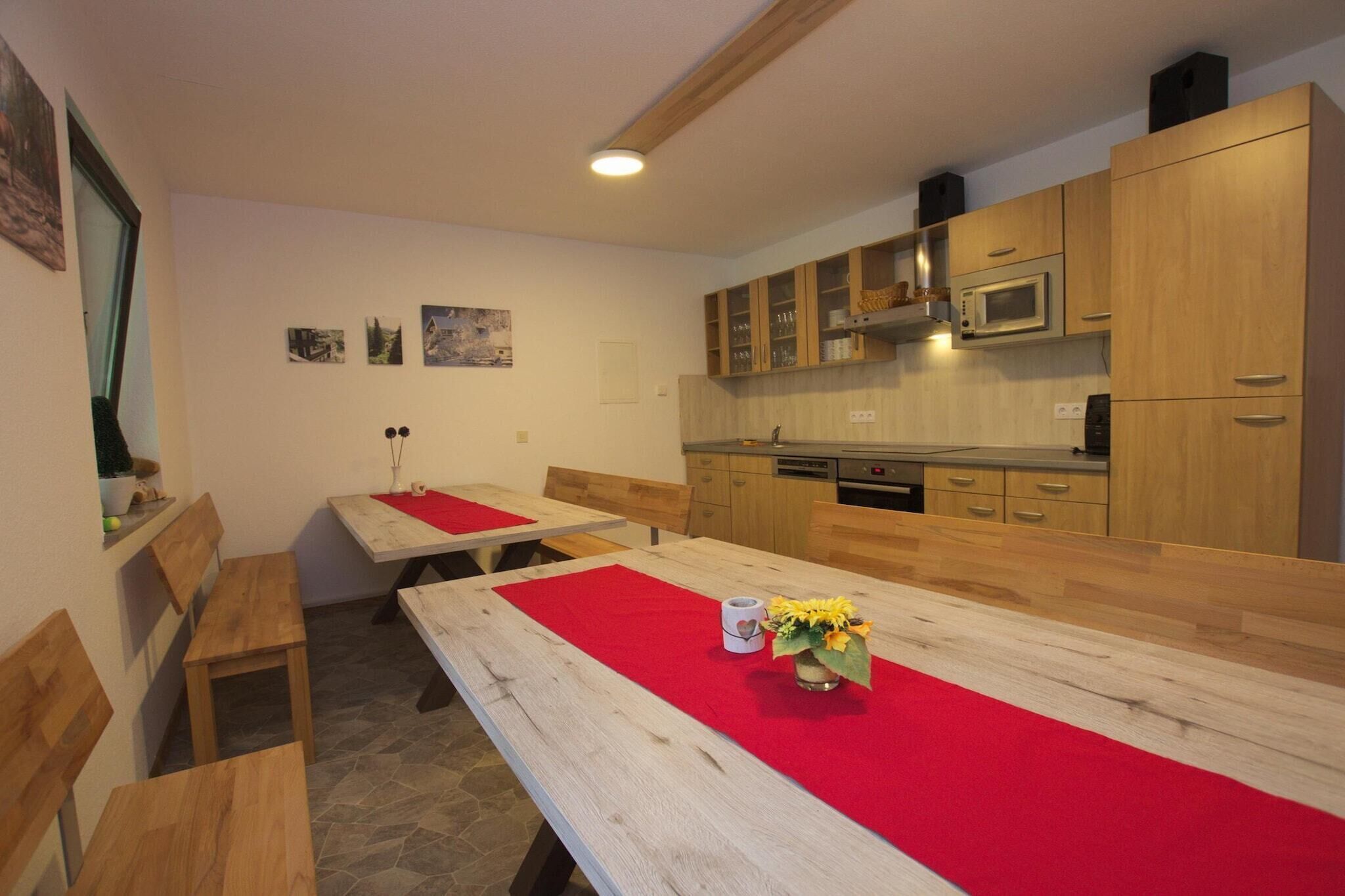 Ein Essbereich mit Holztischen und -bänken, einer roten Tischdecke und einer Vase mit Blumen.