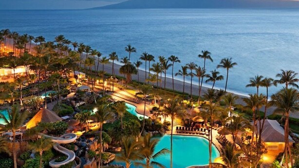 A resort with a large pool, palm trees, and a view of the ocean.