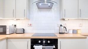 Una cocina moderna con armarios blancos, una estufa negra, un tostador, un hervidor y una cafetera.