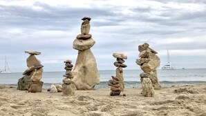 A beach with stacks of stones and a sailboat in the distance. - Villa Blanca views and pool (Níjar)