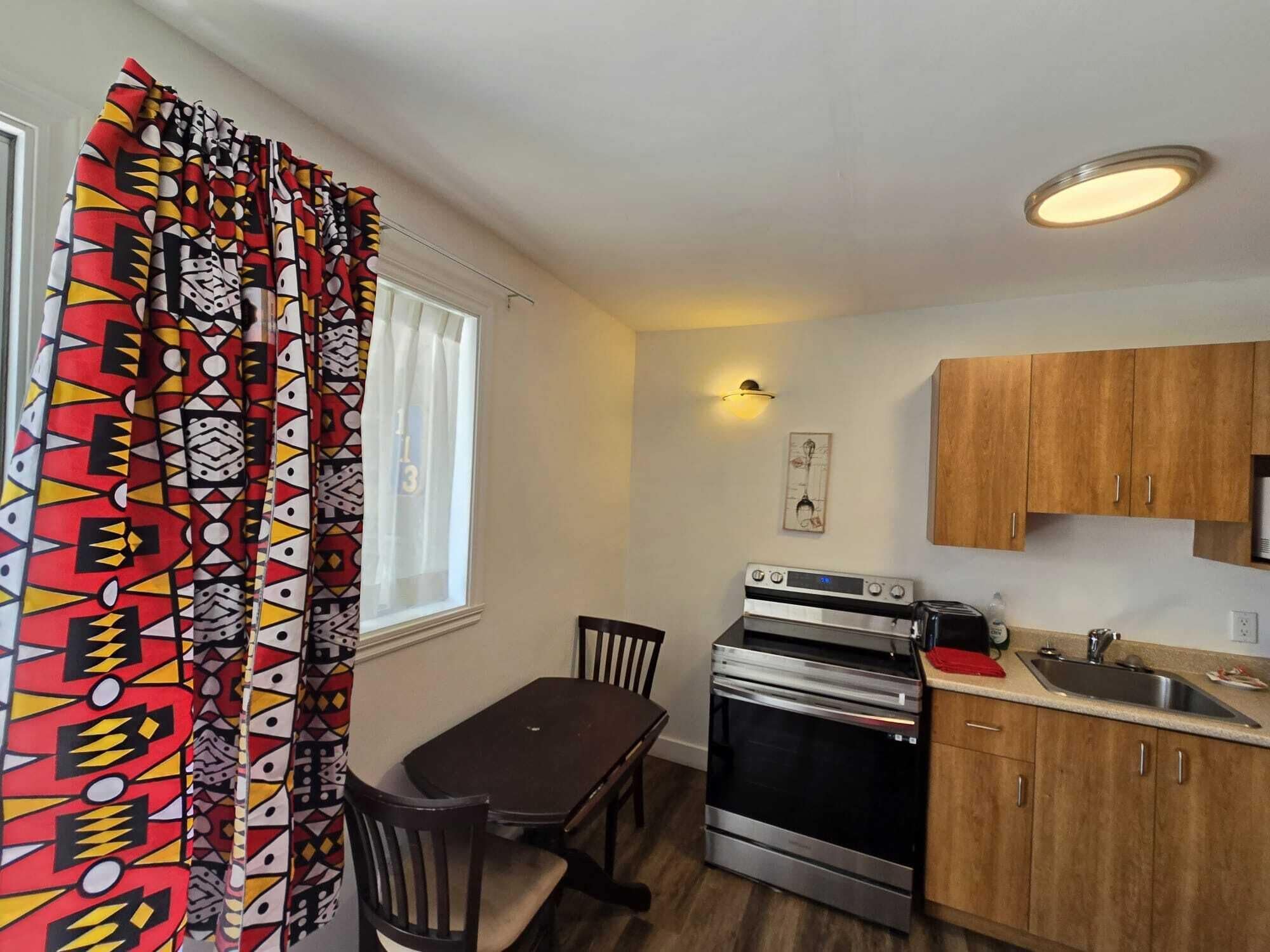 A compact kitchen with a dining table, chairs, a stove, and wooden cabinets.