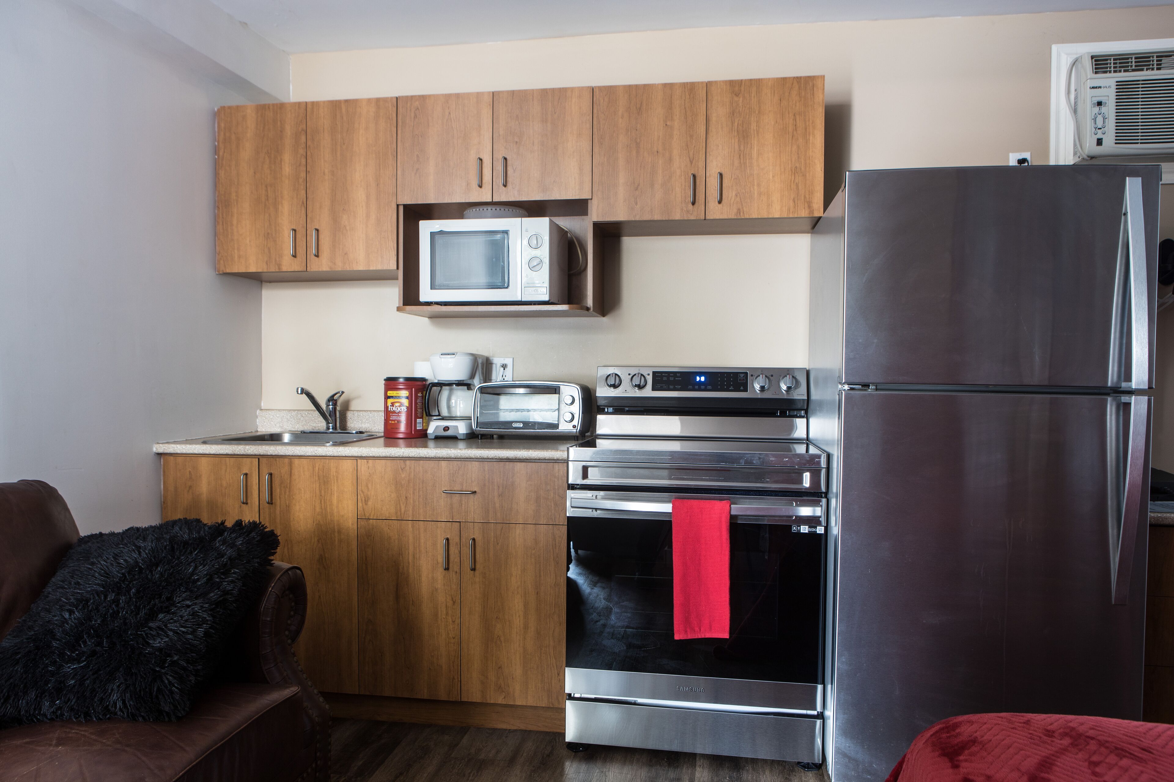 A compact kitchen with wooden cabinets, a microwave, a toaster, a stainless steel refrigerator, and an oven.