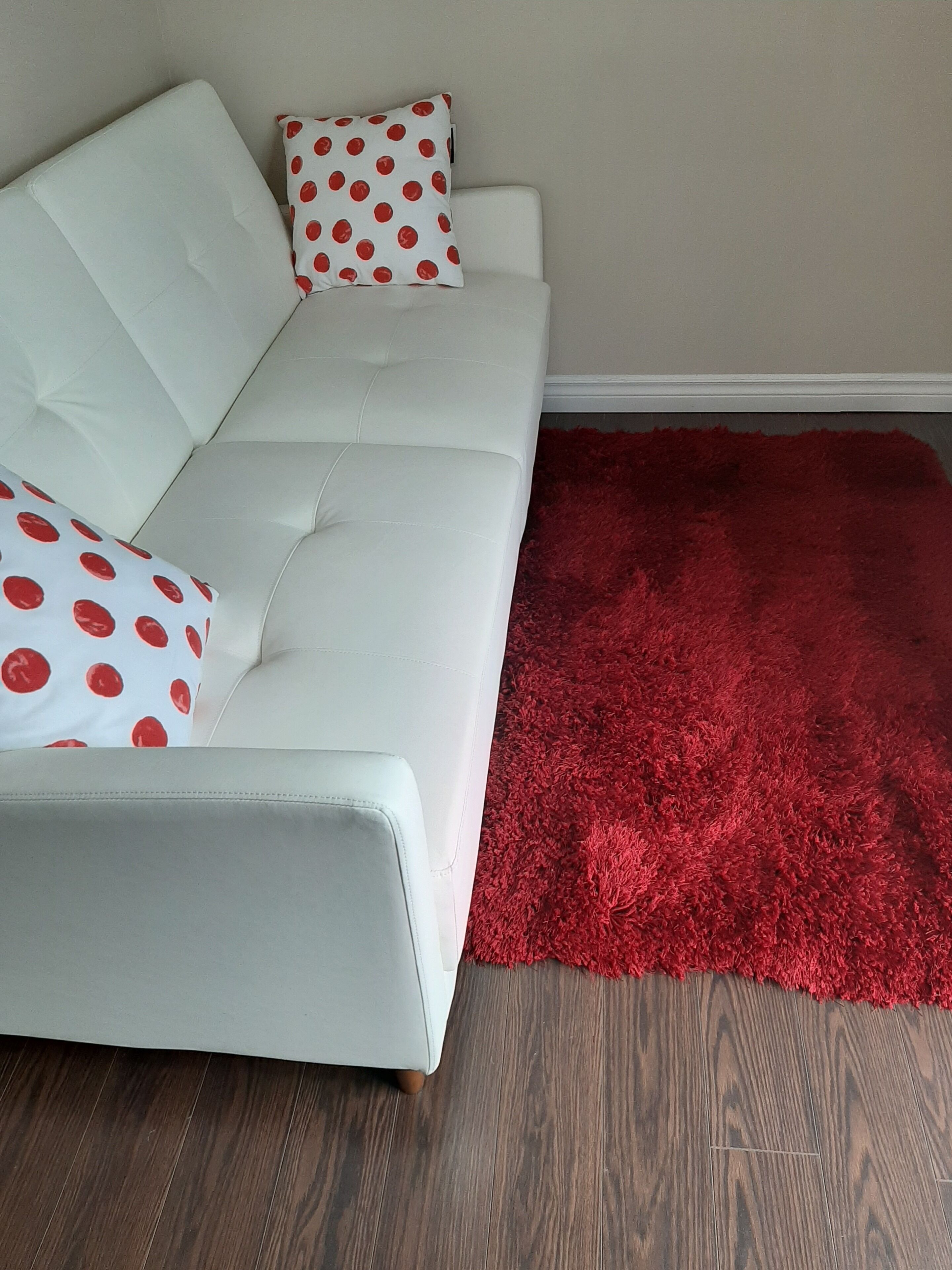 A white sofa with red polka dot pillows and a red shag rug.