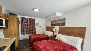 A hotel room with two beds, a TV, a desk, and a window with patterned curtains. - Auberge Motel La Référence (Trois-Rivieres)