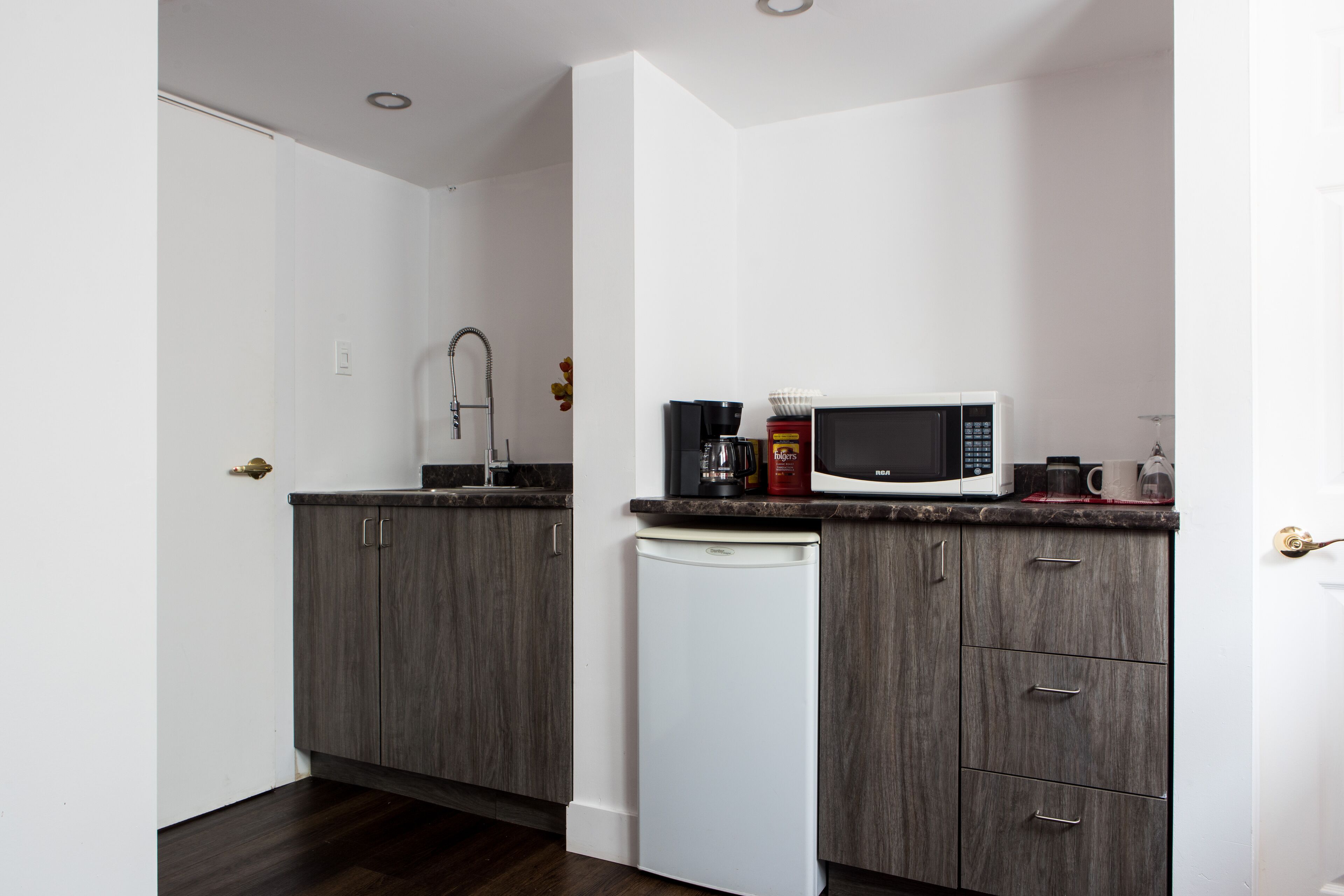 Cocina compacta con alacenas de madera oscura, un refrigerador blanco, un microondas y una cafetera sobre la encimera.