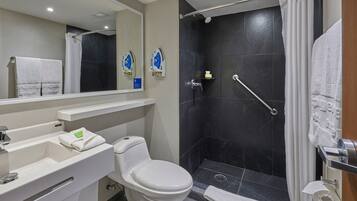 A modern bathroom with a white toilet, a sink with a mirror, and a shower area with a grab bar.